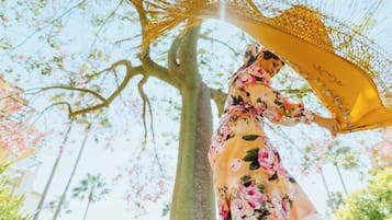 Een vrouw in een bloemenjurk die een gele parasol vasthoudt in een gebied met bomen.