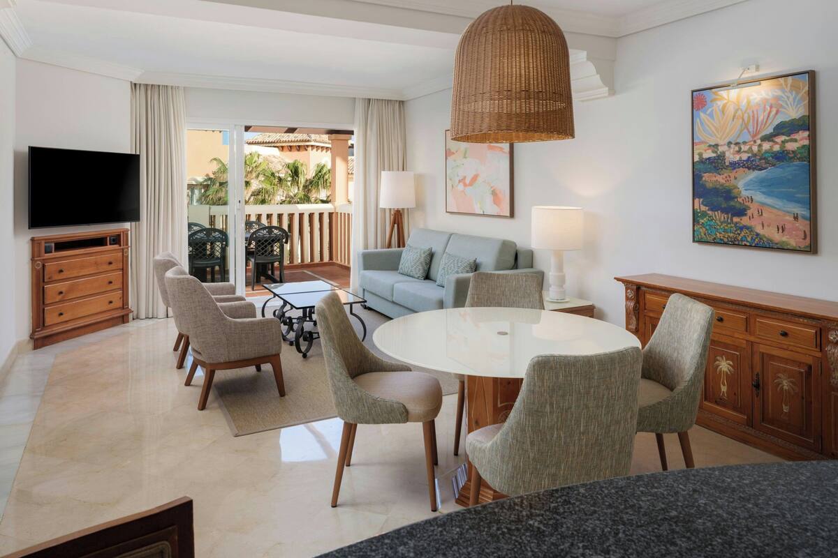 A living room with a TV, sofa, chairs, a dining table, and artwork.