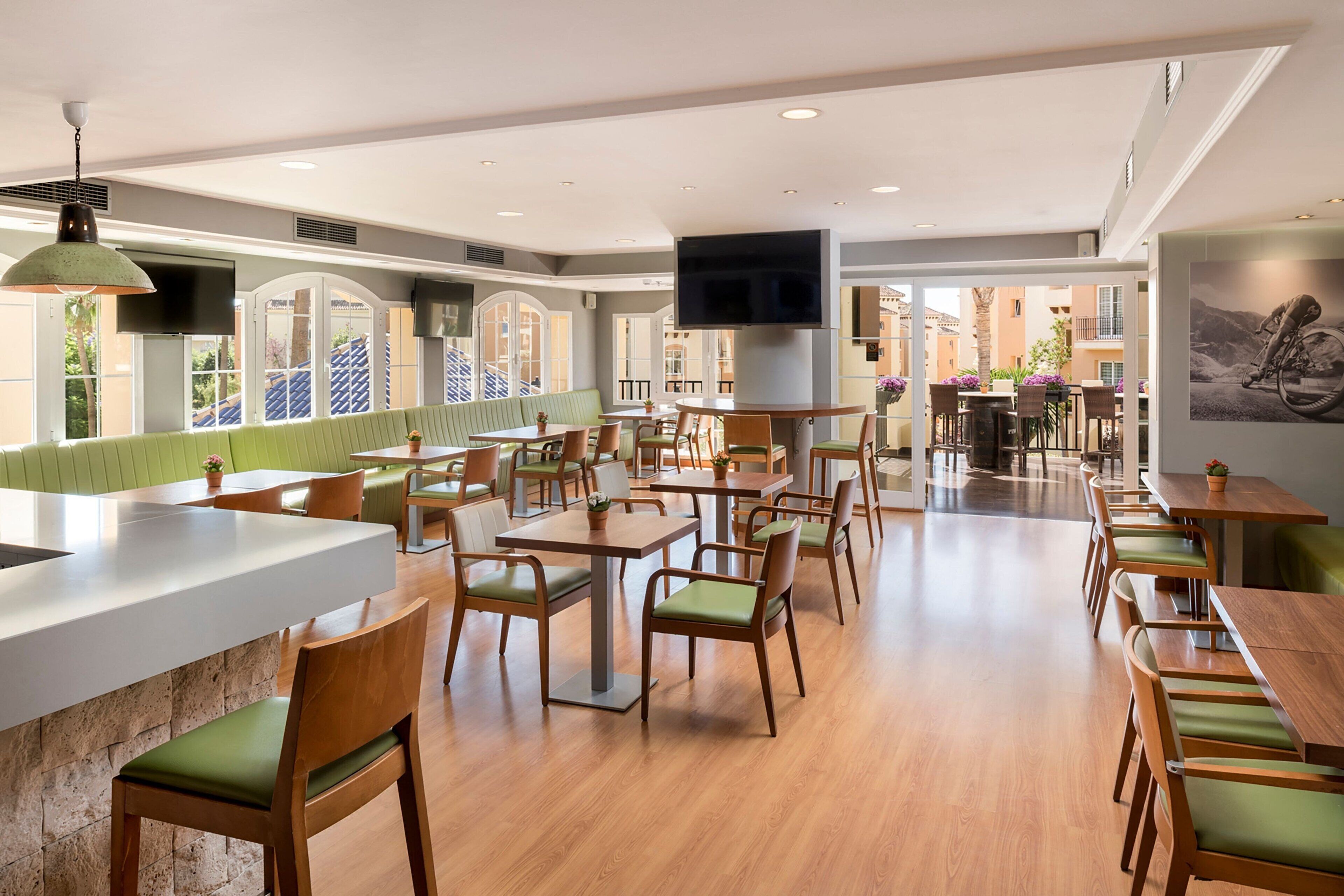 Un grand espace dédié à la salle à manger, avec plusieurs tables et chaises, un grand écran de télévision au centre et une vue sur la terrasse extérieure.