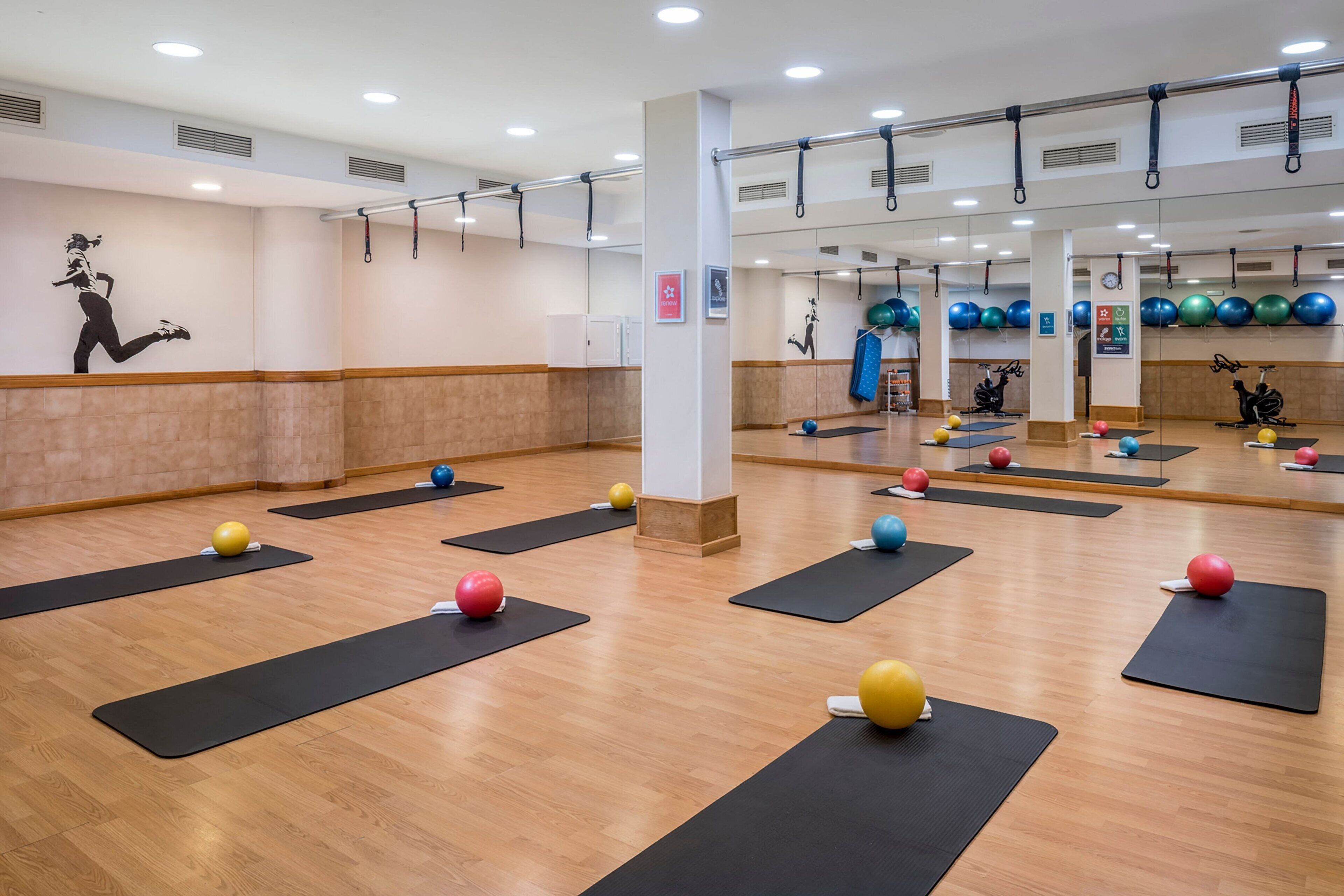 A fitness studio with exercise mats, balls, and a mirrored wall.