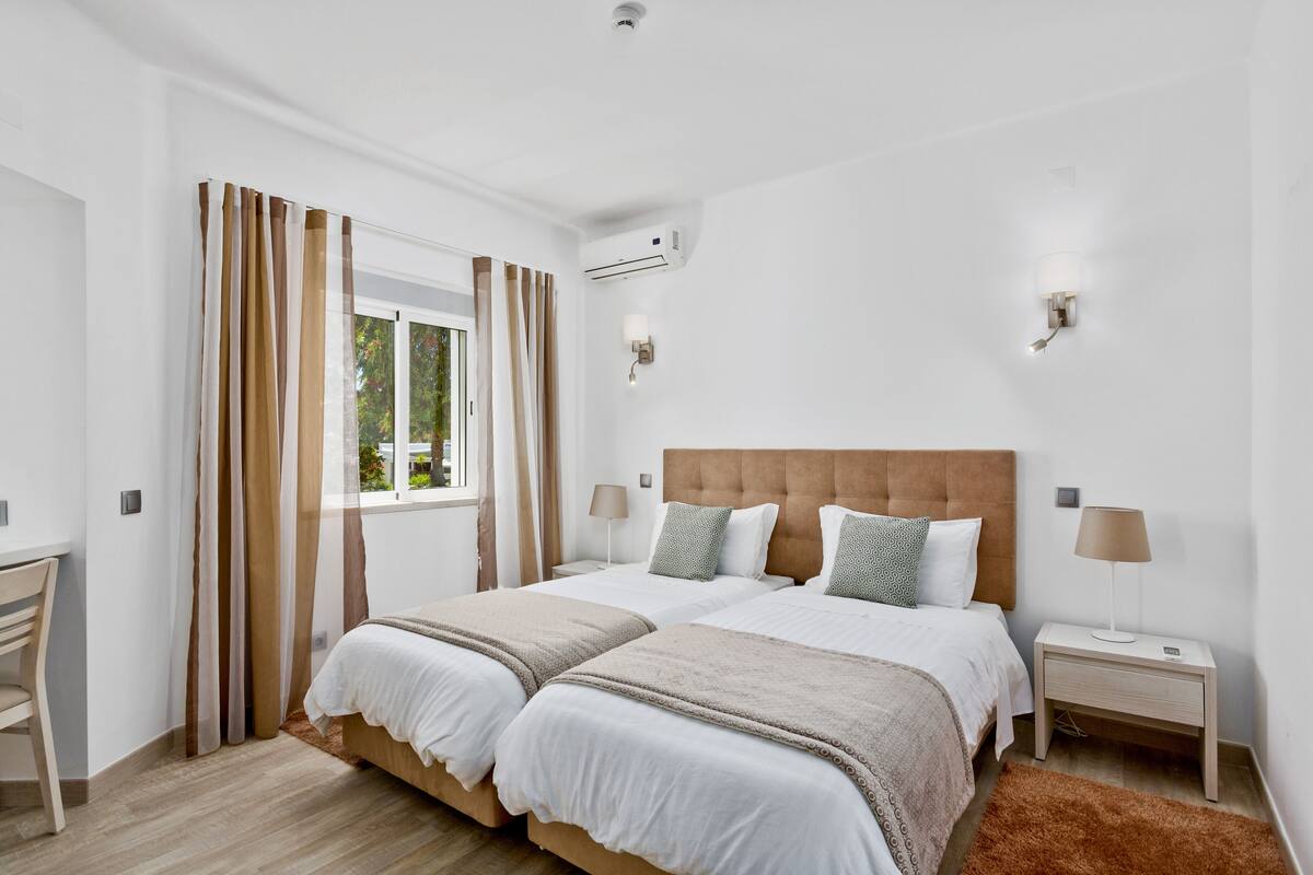 Un dormitorio con dos camas, un escritorio y una ventana con cortinas.