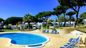 A swimming pool with blue tiles, surrounded by lounge chairs and a stone wall. - Prado Villas (Loulé)