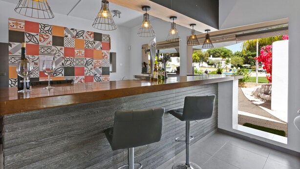 A modern bar area with a wooden countertop, metal pendant lights, and two bar stools. - Prado Villas (Loulé)