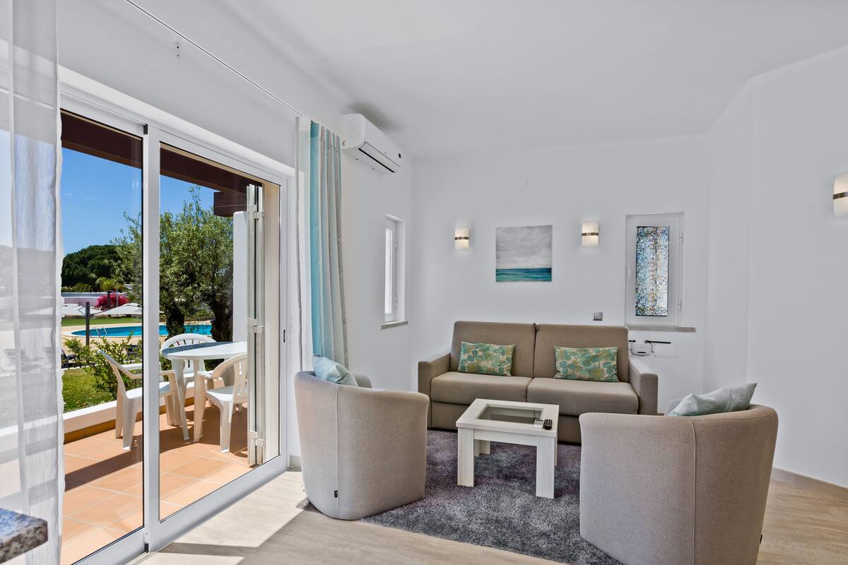 Una sala de estar moderna con un sofá, dos sillones, una mesa de centro y un ventanal de vidrio que da a un área exterior con piscina.