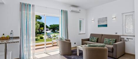 Een moderne woonkamer met een bank, fauteuils en een salontafel. Er is een glazen schuifdeur naar een buitenruimte met een zwembad en groen.