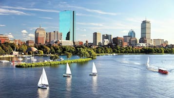 Un horizonte urbano con edificios modernos, un río con veleros y un parque con árboles.