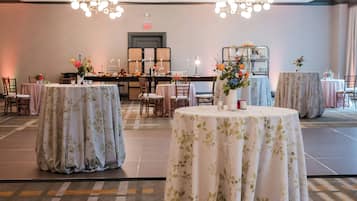 A banquet hall with round tables covered in floral tablecloths, a buffet setup, and a chandelier.