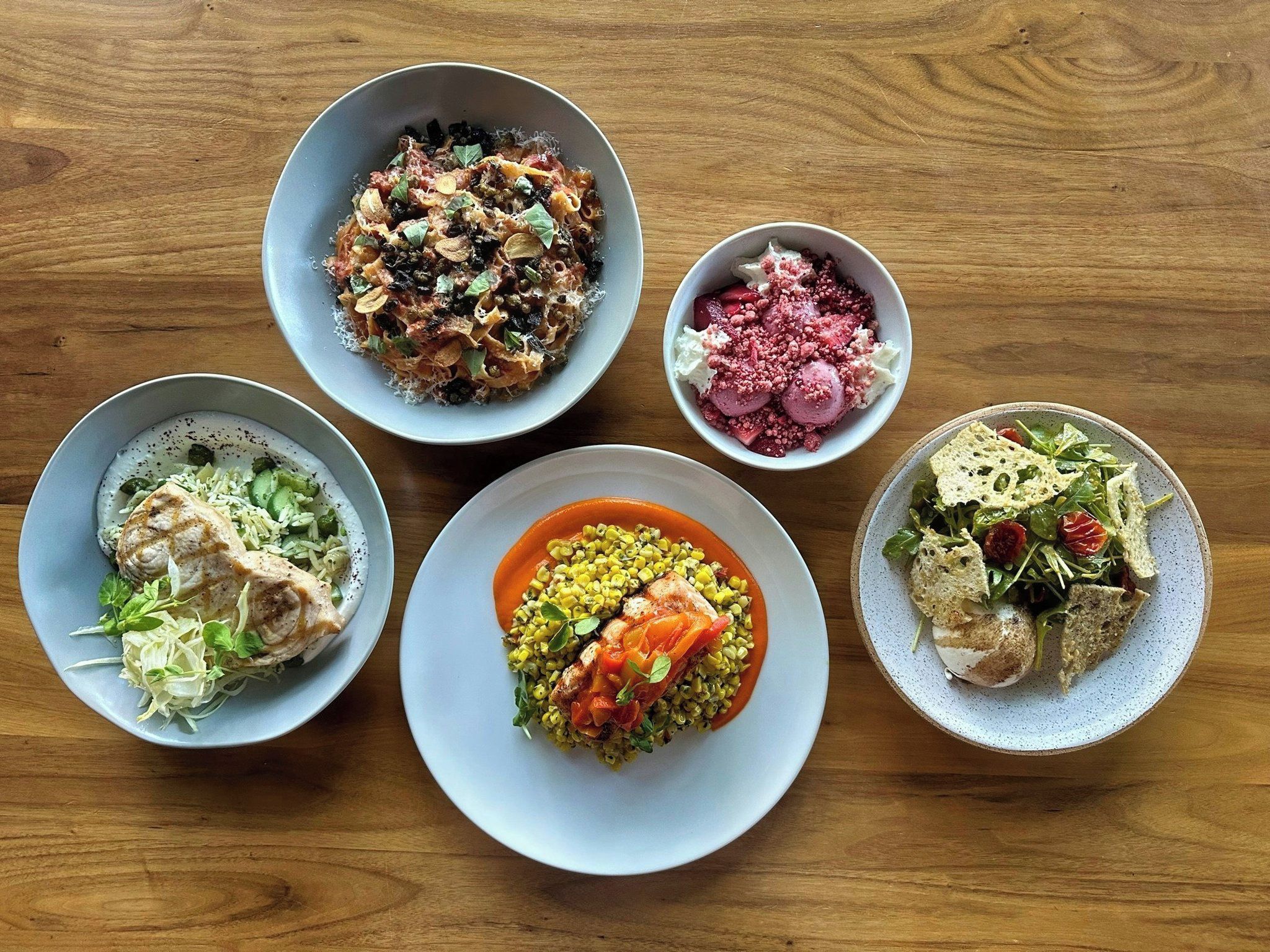 A wooden table with five bowls of food.