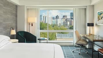 Une chambre d’hôtel équipée d’un lit, d’un bureau, d’une chaise, d’une lampe et d’une grande fenêtre donnant sur la ville.