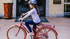 A woman riding a red bicycle with a basket in front of a building with a sign that reads "KIMPTON Hotels & Restaurants." - Kimpton Marlowe Hotel by IHG (Cambridge)