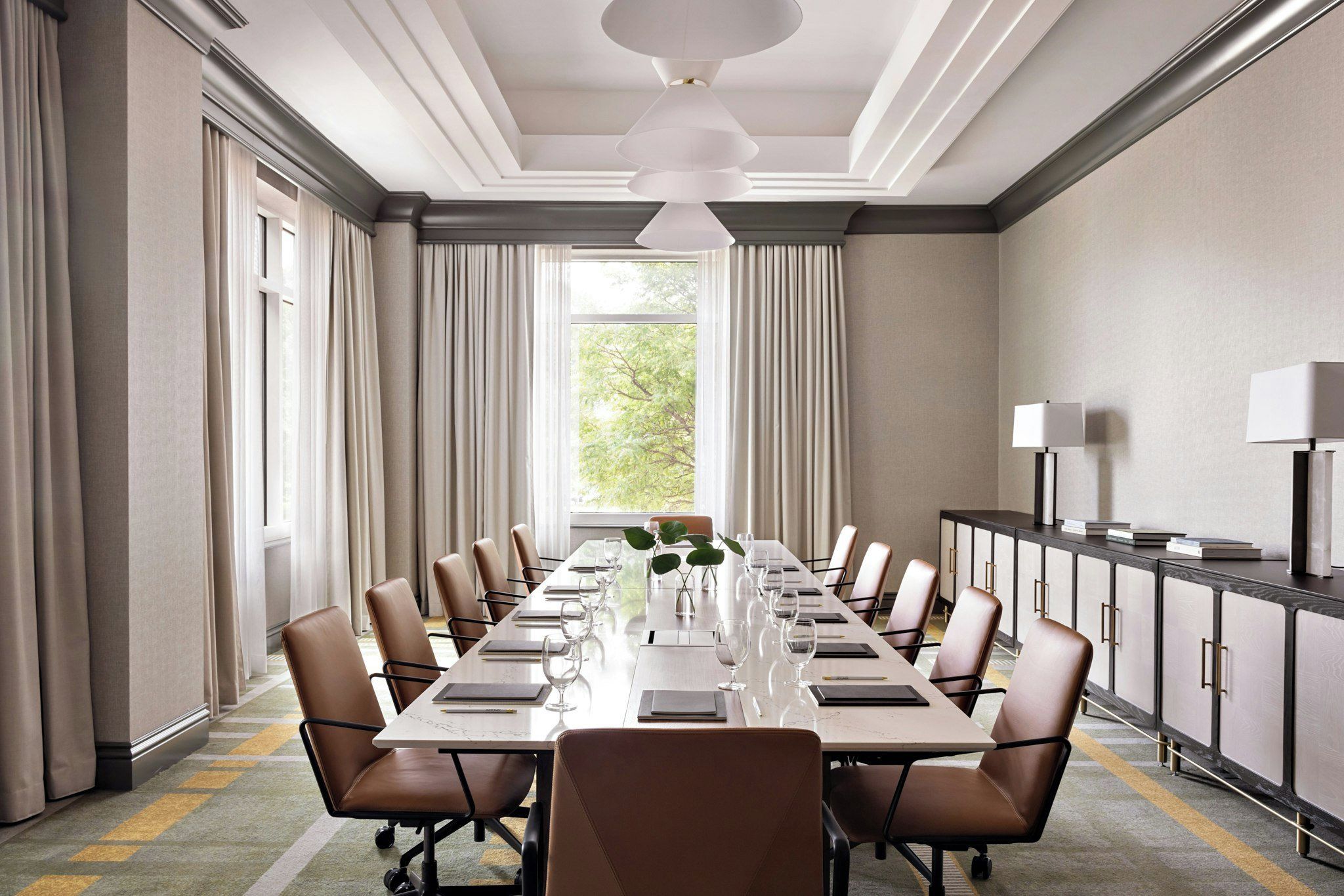 A conference room with a long table, chairs, a plant, and a cabinet with a lamp.