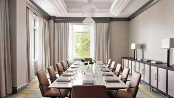 A conference room with a long table, chairs, a plant, and a cabinet with a lamp.