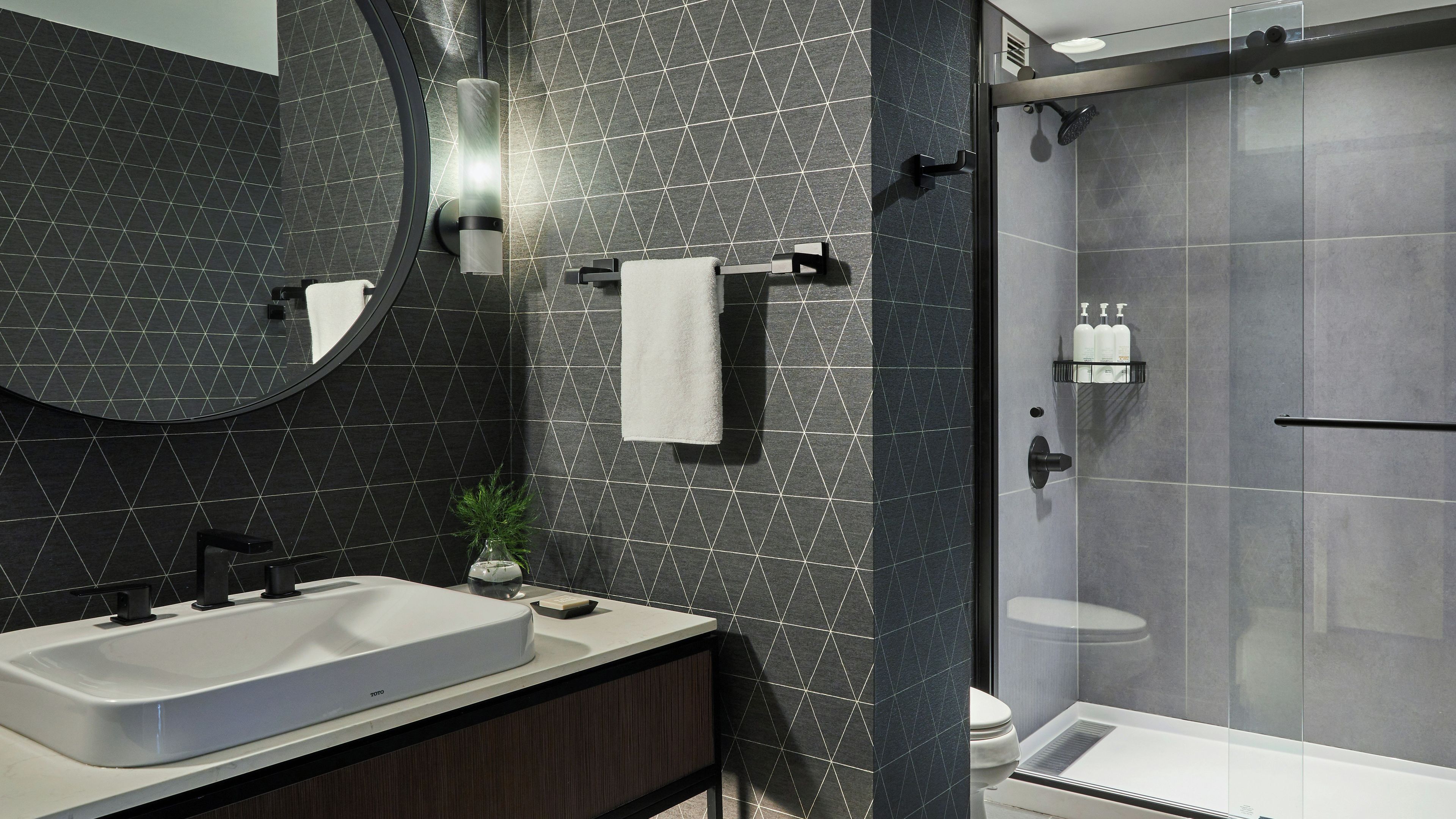 Un baño moderno con un espejo grande, un lavamanos, una ducha y un inodoro.