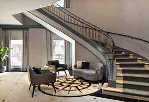 A modern interior with a curved staircase, a seating area with a round coffee table, and a large window providing natural light. - Kimpton Marlowe Hotel by IHG (Cambridge)