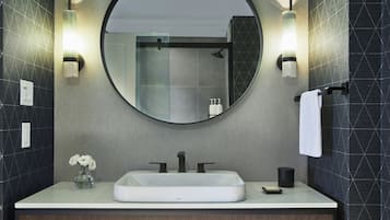 Une salle de bain moderne avec un miroir rond, un lavabo blanc et deux appliques murales.
