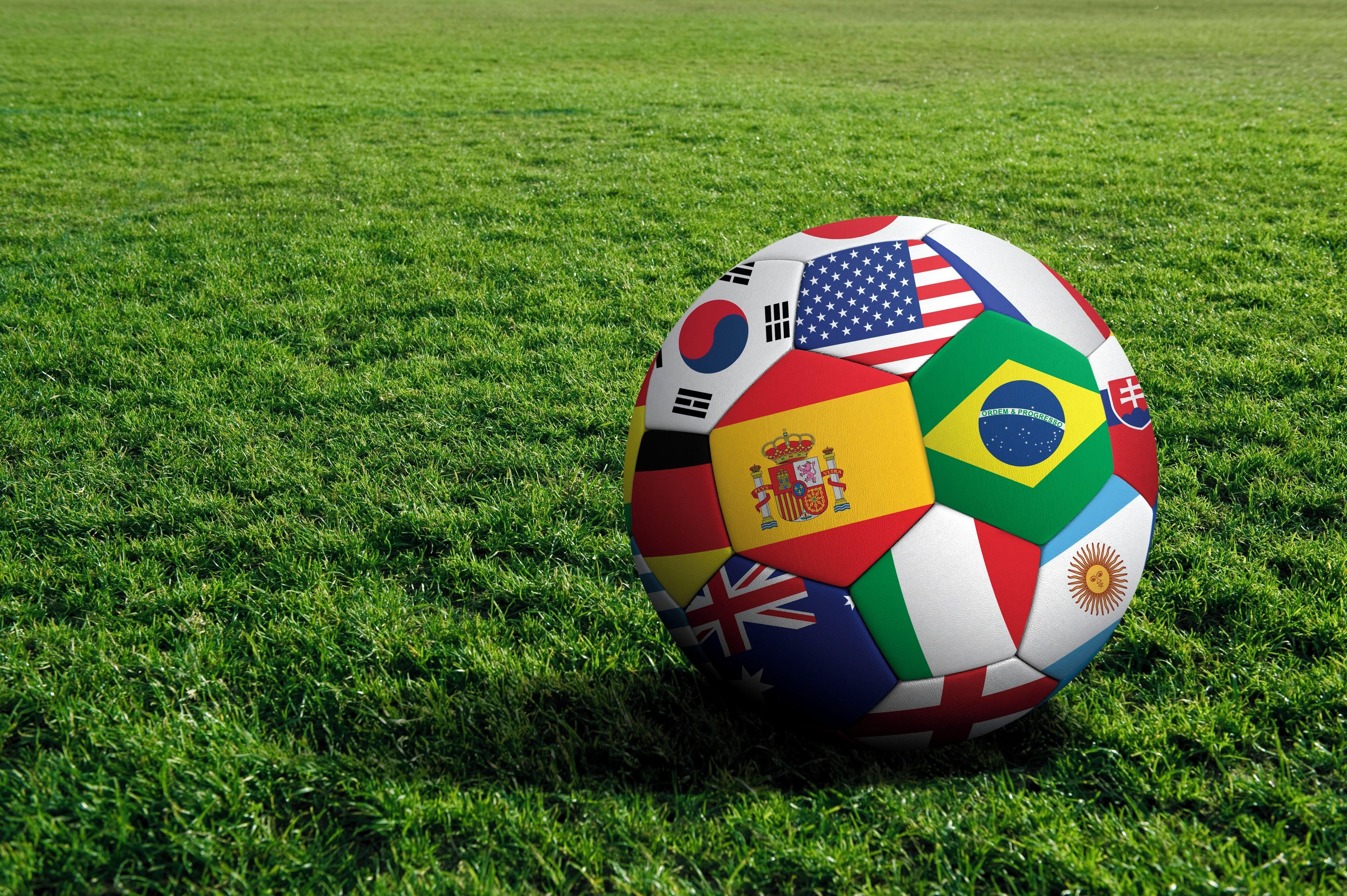 Un balón de fútbol con varias banderas nacionales sobre un campo de césped.