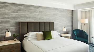 A hotel room with a large bed, two bedside tables, a green chair, and a window with curtains.