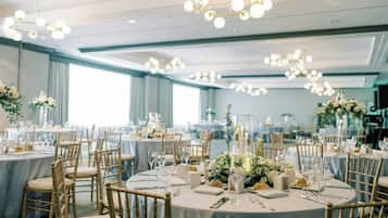 Een feestzaal met ronde tafels, stoelen en kroonluchters.