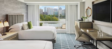Habitación de hotel con dos camas, un escritorio, una silla, un televisor y vista a la ciudad.