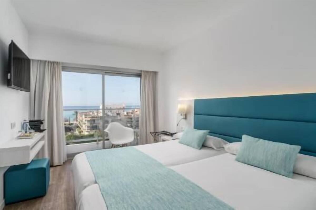 A hotel room with a bed, a desk, a chair, and a view of the city.