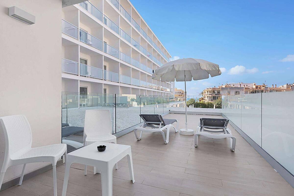 A balcony with white chairs, a table, and an umbrella.
