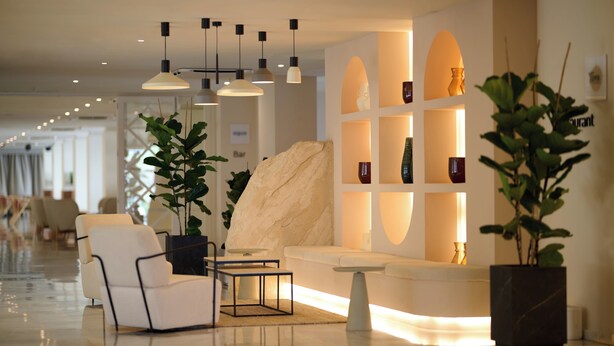 A modern lobby with a sofa, chairs, a coffee table, pendant lights, and potted plants.