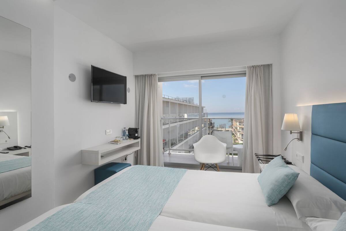 A hotel room with a bed, a desk, a chair, a TV, and a balcony with a view.