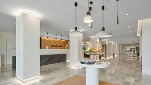 A modern hotel lobby with a reception desk, pendant lighting, and a central round table with glassware.