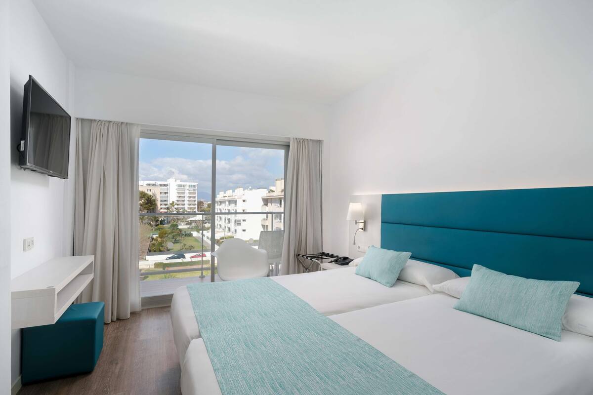 A modern hotel room with a large bed, a desk, a chair, and a TV.