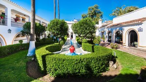 Un patio con una fuente central, rodeado de setos cuidados y palmeras.