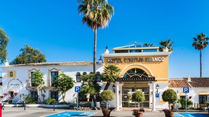 Un hotel con una entrada destacada, un área de estacionamiento y varias plantas en macetas.