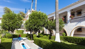 A courtyard with a fountain, palm trees, and a building with balconies. - Globales Cortijo Blanco (Marbella)