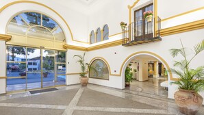 Un vestíbulo de hotel con una entrada imponente, varios arcos y plantas en macetas.