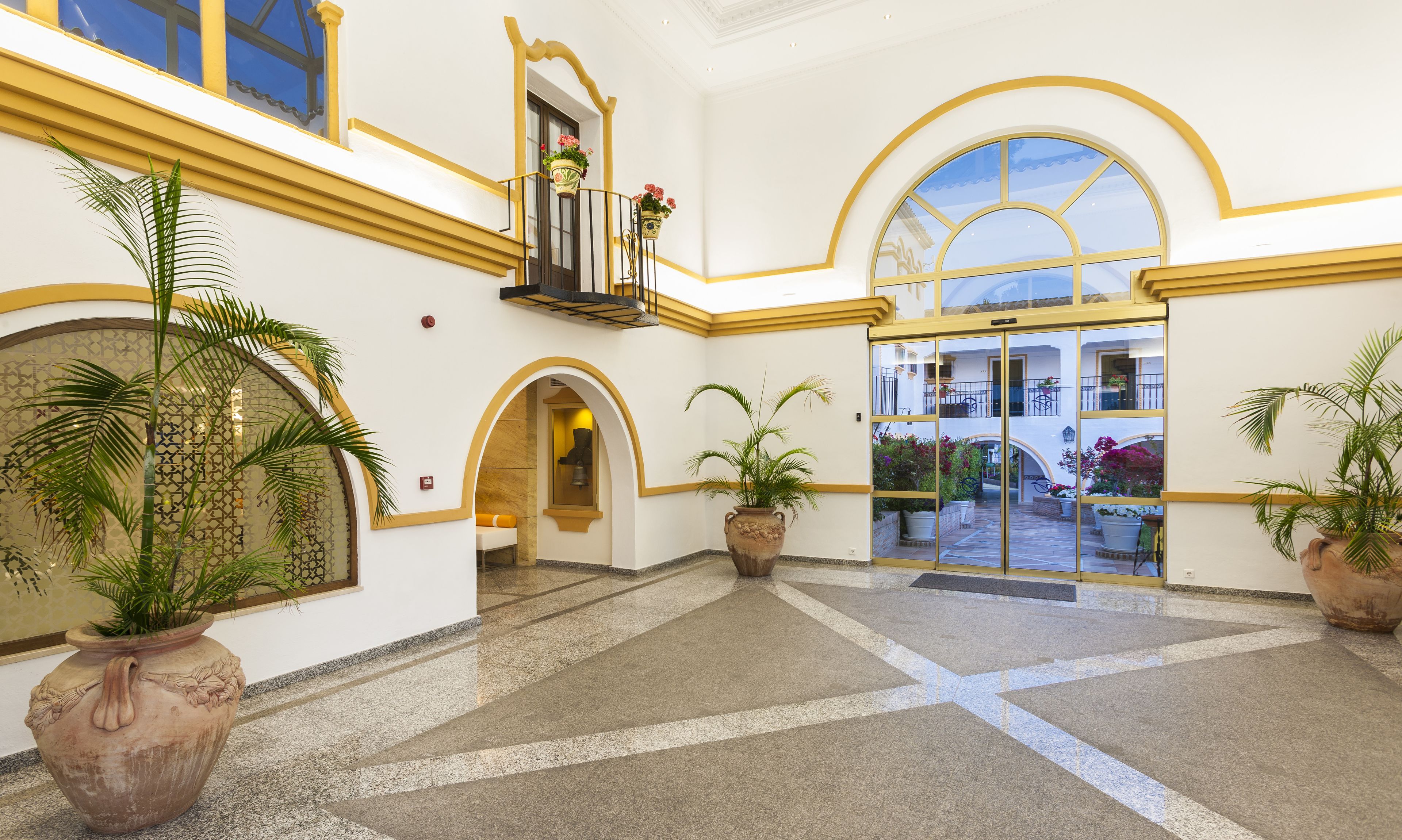 Un vestíbulo amplio con techo alto, plantas en macetas grandes y una zona central abierta con vista al patio.