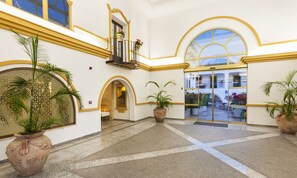 A spacious lobby with a high ceiling, large potted plants, and a central open area with a view of the courtyard. - Globales Cortijo Blanco (Marbella)