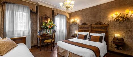 A hotel room with a large bed, a desk with a chair, a chandelier, and wall sconces.