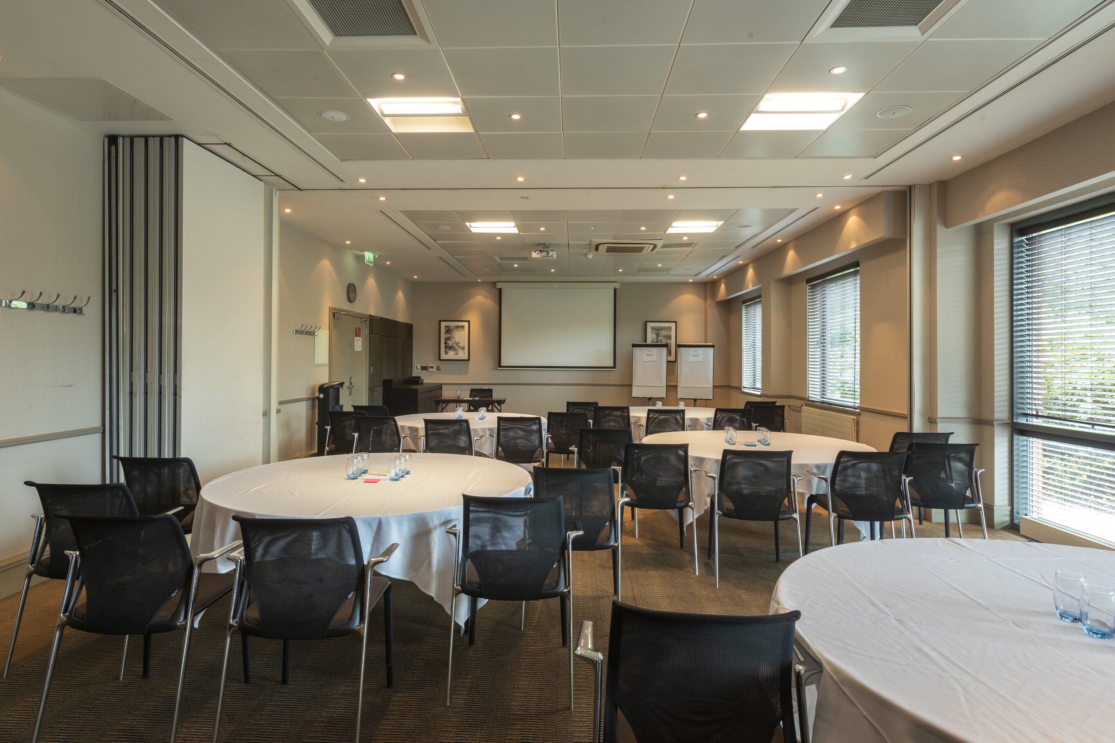 A conference room with multiple round tables, black chairs, and a projector screen.