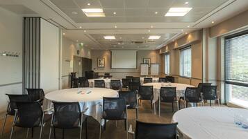 A conference room with multiple round tables, black chairs, and a projector screen.