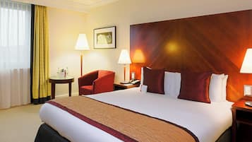 Habitación de hotel con una cama grande, dos mesitas de noche, una silla, una lámpara y un cuadro en la pared.