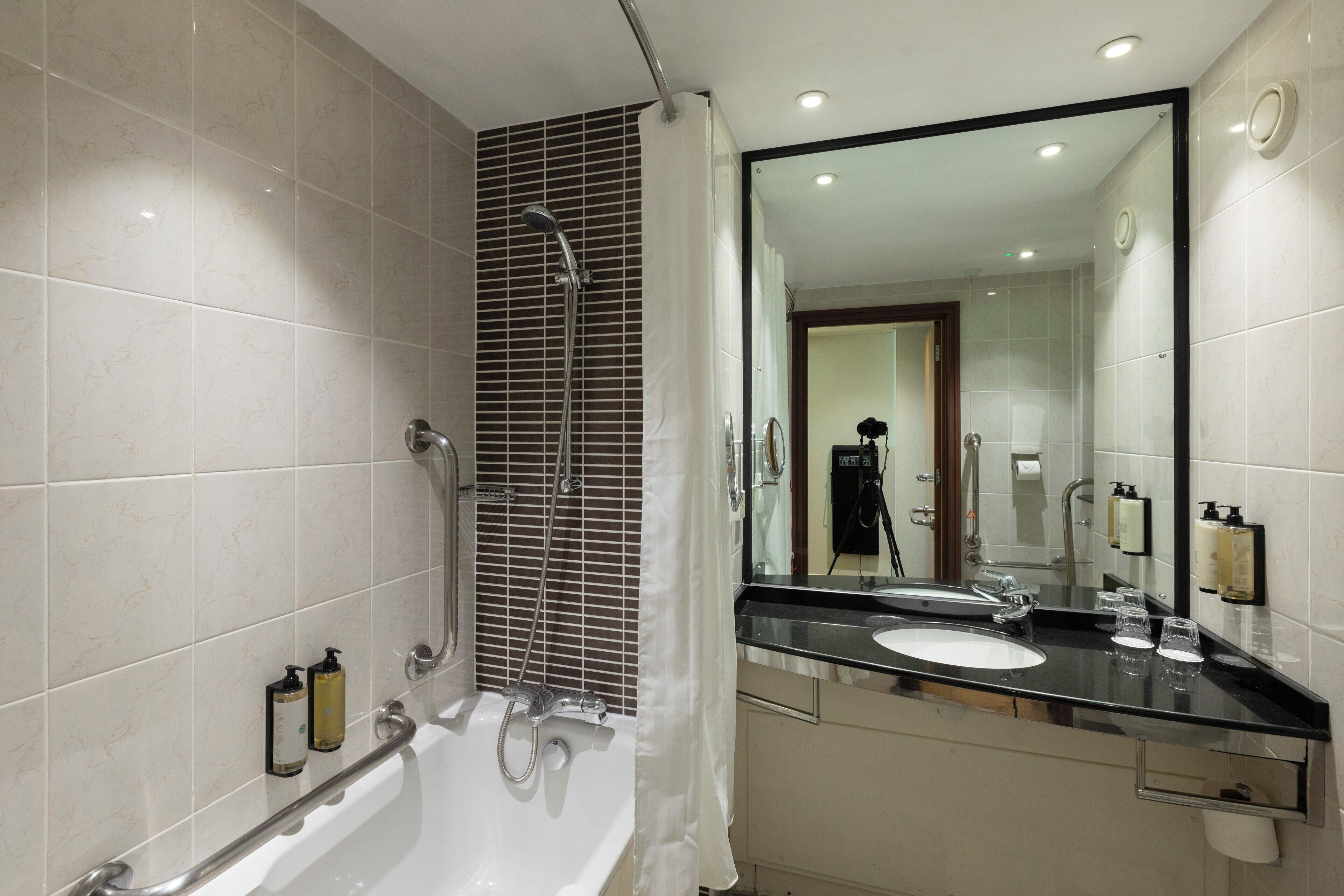 Een moderne badkamer met een badkuip, douche, grote spiegel en wastafel.