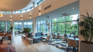 A spacious, well-lit lounge area with a curved ceiling, large windows offering views of greenery, and a variety of seating options including sofas, chairs, and a dining table. - Crowne Plaza Birmingham NEC by IHG (Birmingham)