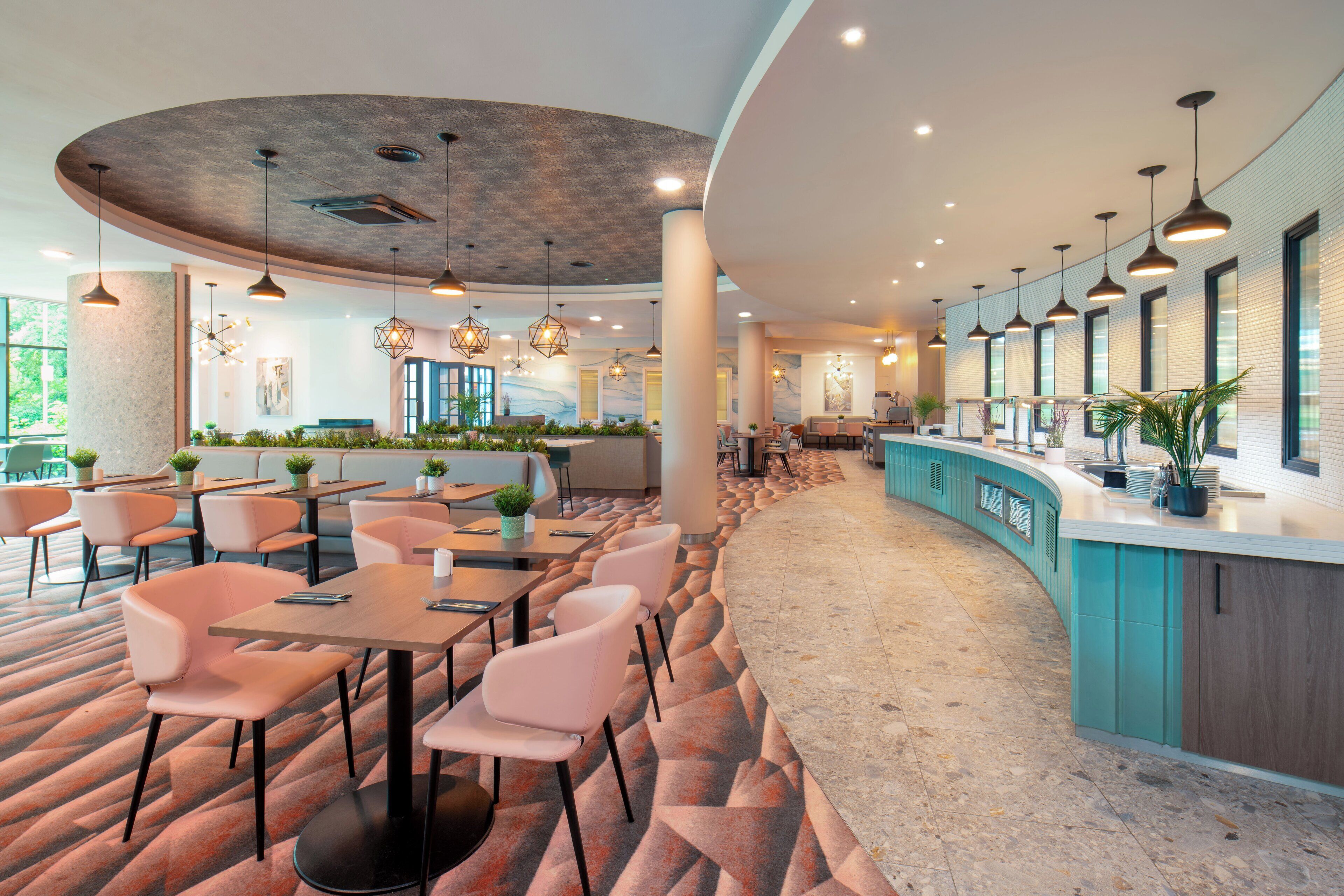 Un restaurant moderne doté d’un comptoir incurvé, de plusieurs espaces de restauration et d’un éclairage suspendu.