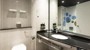 A modern bathroom with a white toilet, a glass shelf with towels, a black sink, and a mirror with a cityscape design.
