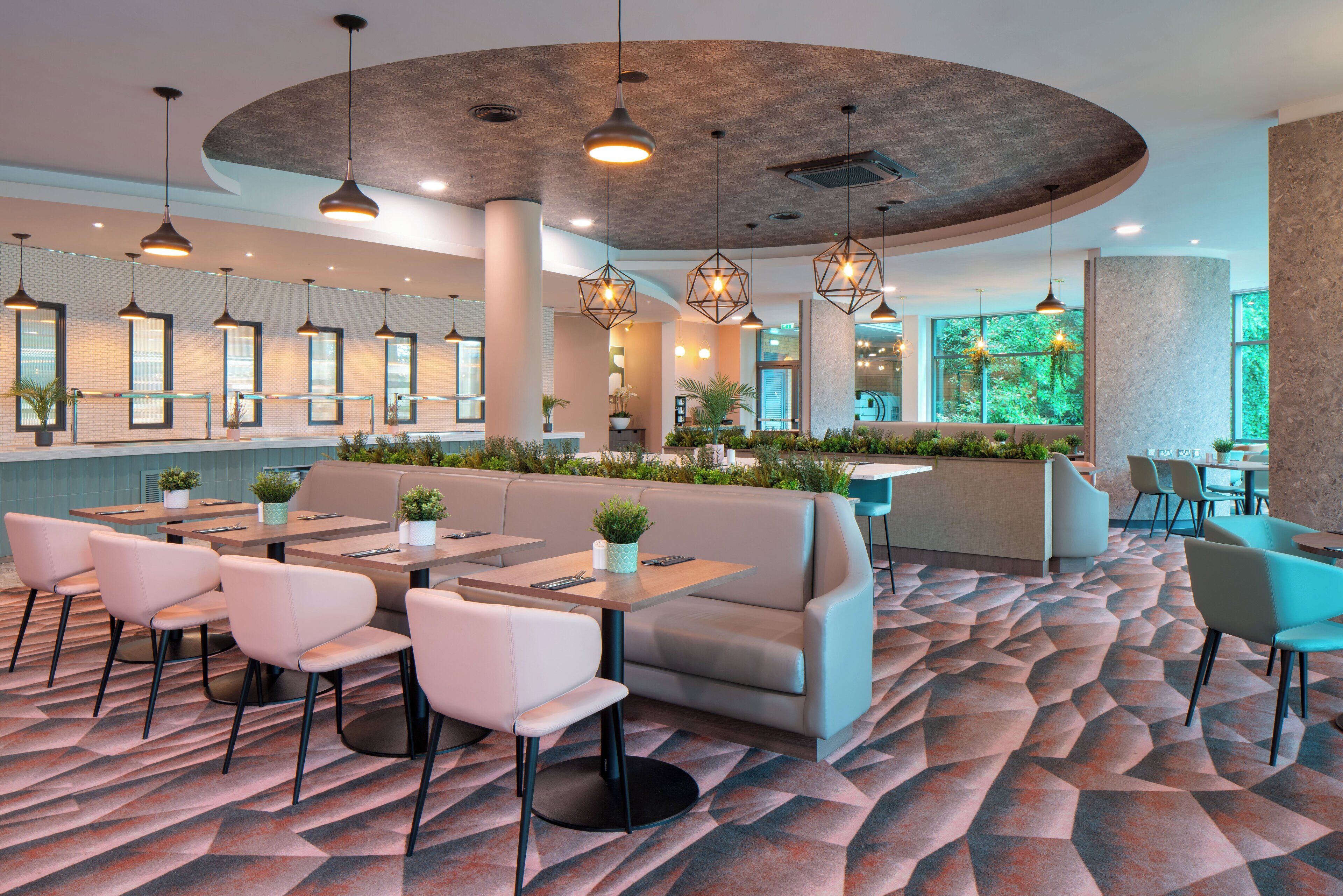 A modern restaurant with a curved ceiling, pendant lighting, and a patterned carpet.