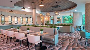 A modern restaurant with a curved ceiling, pendant lighting, and a patterned carpet.