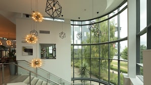 A modern interior with a curved glass railing, geometric pendant lights, and a view of greenery outside. - Crowne Plaza Birmingham NEC by IHG (Birmingham)