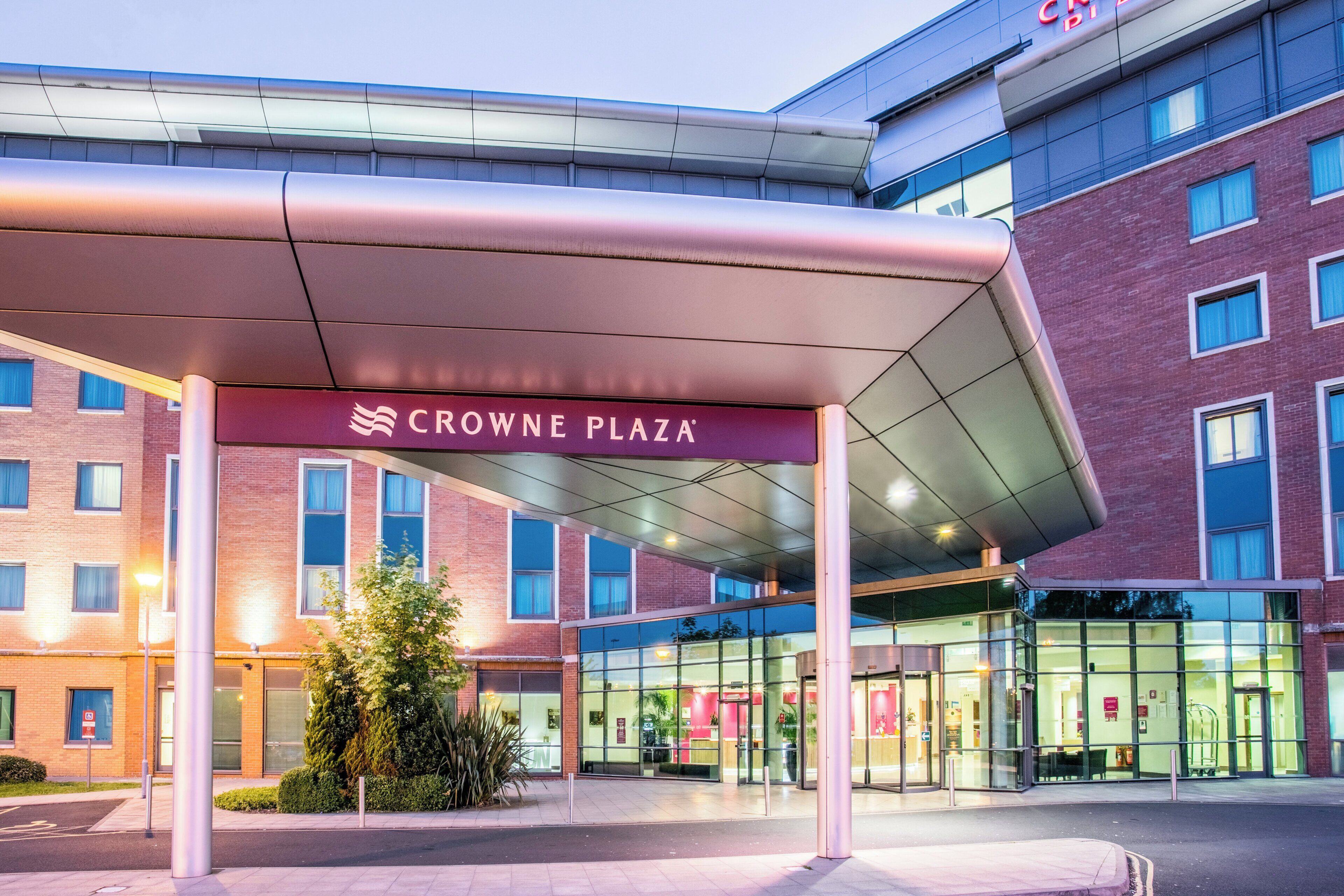 A hotel entrance with a covered walkway, glass doors, and a sign reading 'CROWNE PLAZA'.