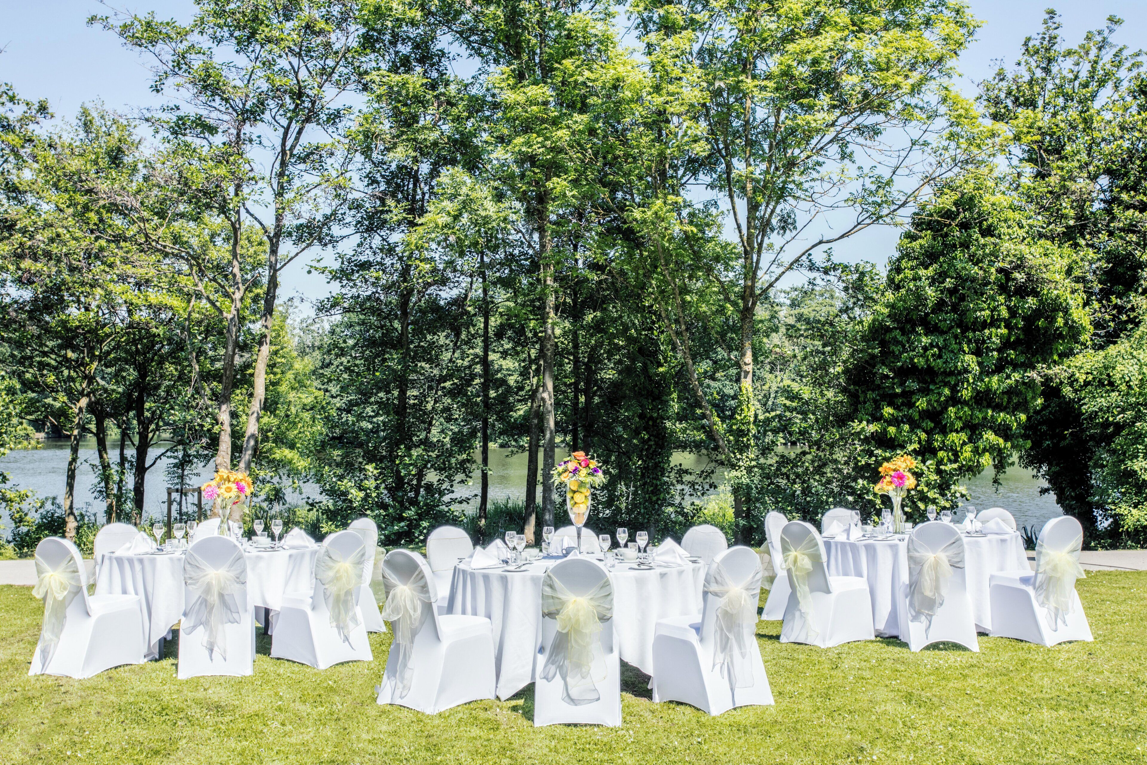 Un espace de restauration en plein air avec des tables rondes, des nappes blanches et des chaises recouvertes de housses blanches.