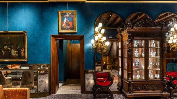 A room with a blue wall, wooden ceiling beams, a large mirror, and a glass cabinet with various items. - Hotel Palazzo Priuli (Venice)