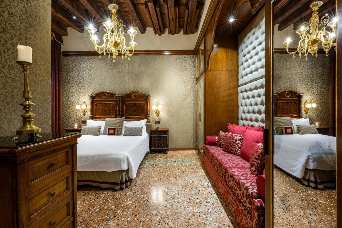 A hotel room with a large bed, a sofa, a dresser, and a mirror.